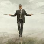 Man in suit walking a tight rope high in the misty air