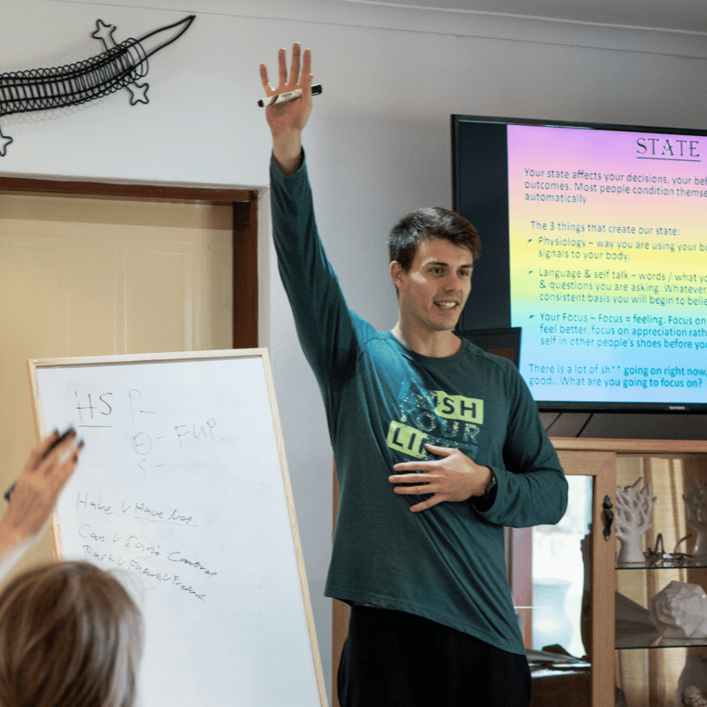 Master coach Rory O Sullivan from Ignite Co presenting a life coaching workshop raises his arm with a screen in the background which shows the theme of his workshop